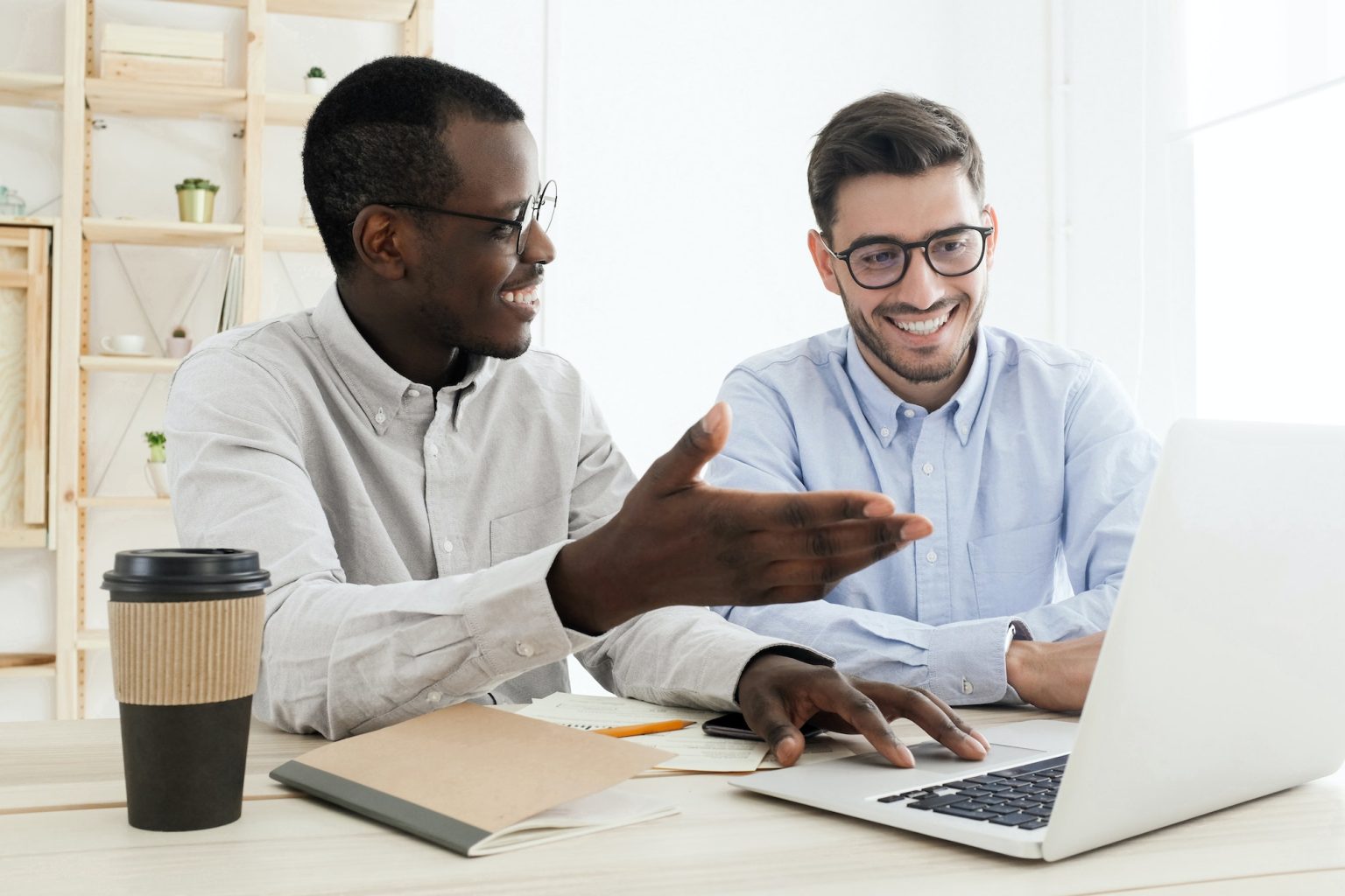 Diverse businessmen using laptop together, african coworker showing something at laptop screen